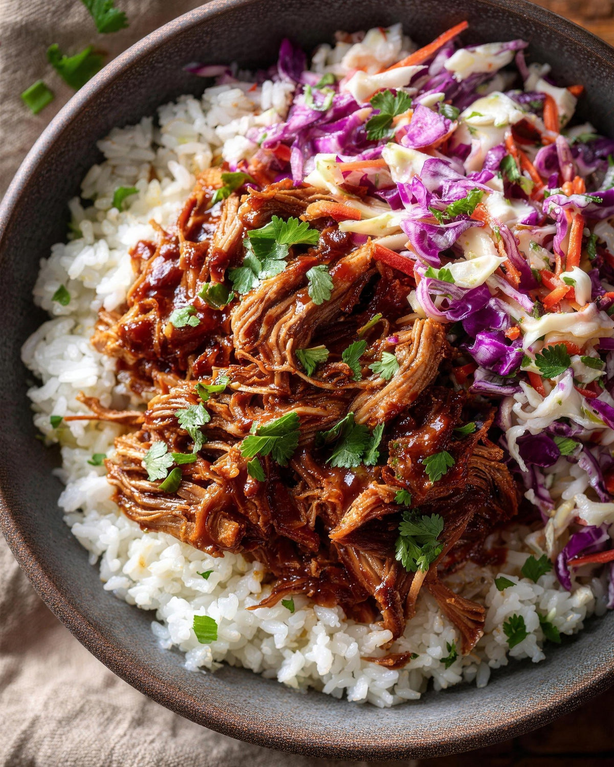 A bowl of sticky BBQ pulled pork and purple cabbage slaw over fluffy white Qetoe Rice, topped with coriander