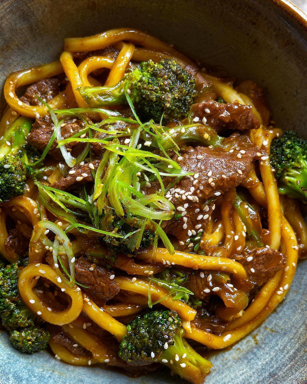 A bowl of low carb beef and broccoli noodles with thick udon-style Qetoe noodles, spring onion and sesame seeds